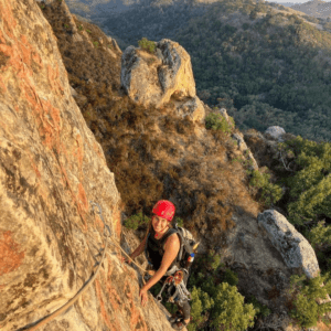 A woman smiles while climbing a rock face with the sunset behind her