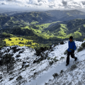 A man walks in the snow while viewing green valleys below in Mt. Diablo State Park