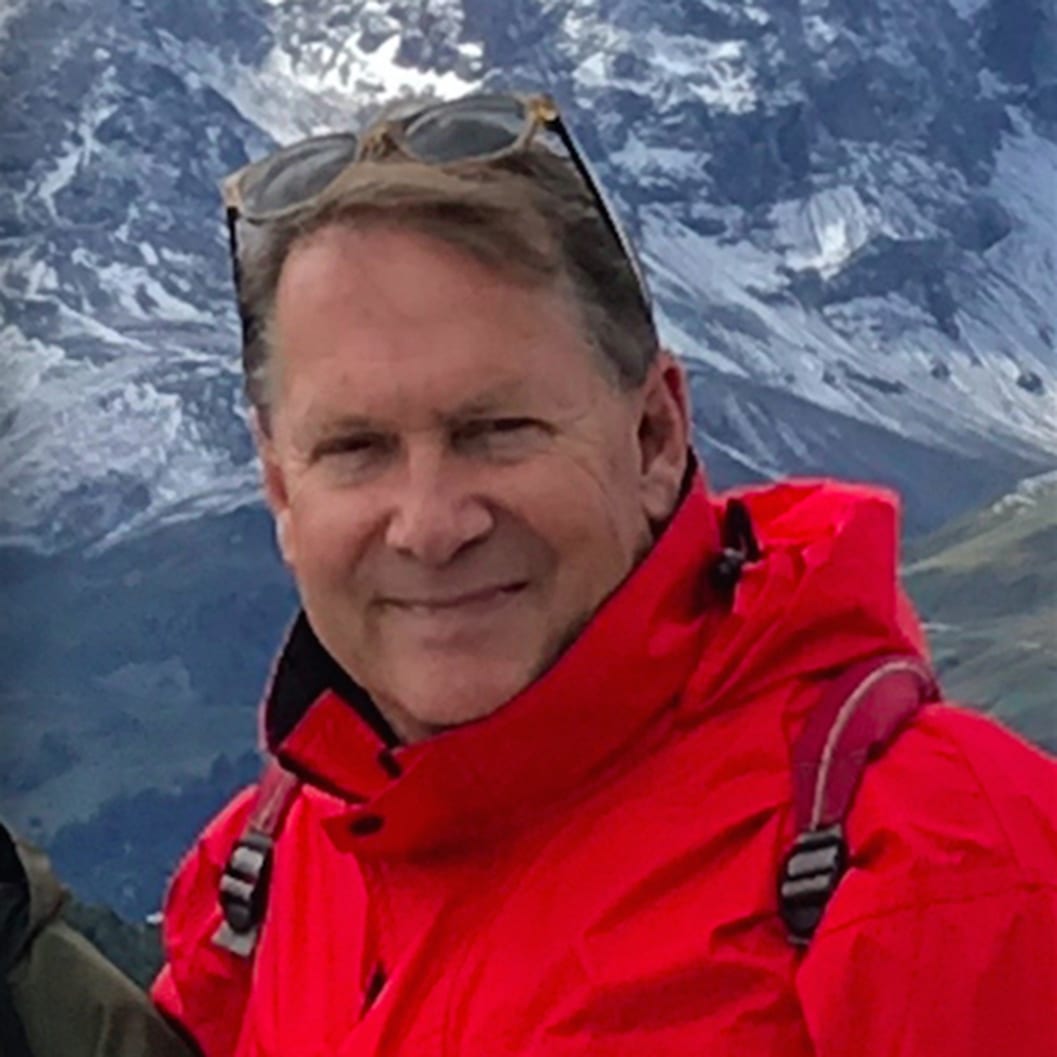 Close up image of Patrick Hunt posing in red jacket in front of mountain range