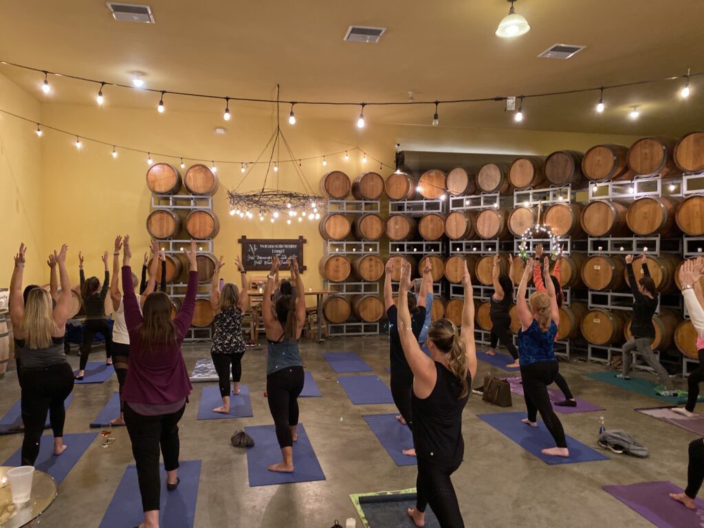 a group of people stand in a yoga pose in the McGrail Vineyards barrel room