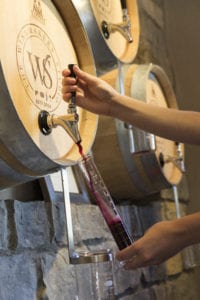 a beaker filling with wine from a barrel in the wall