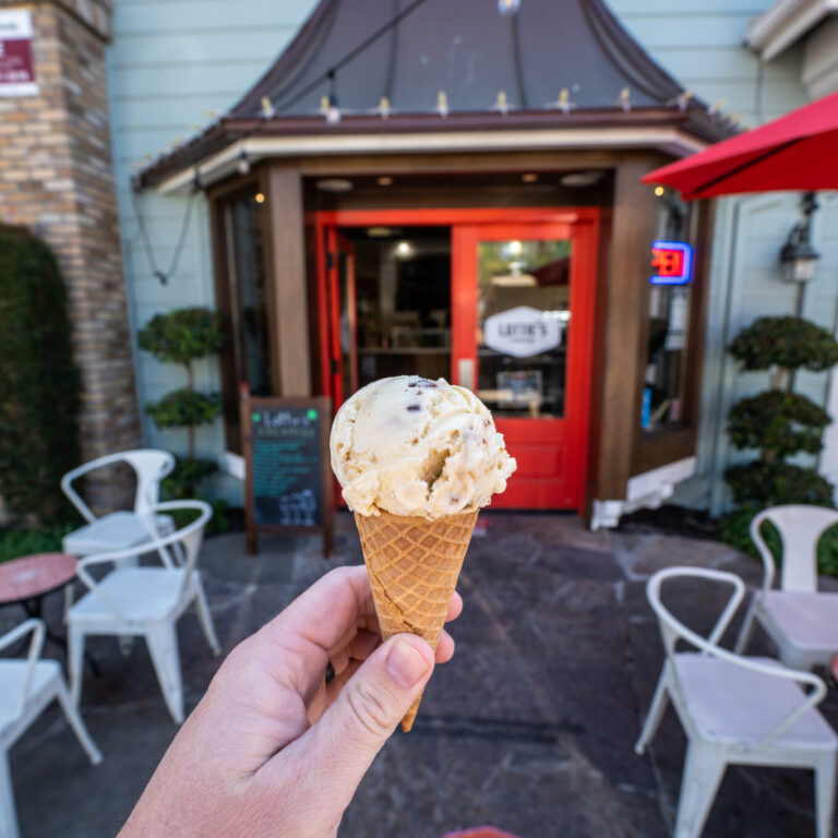 Hand holding a scoop of cookie dough ice cream in a waffle cone in front of Lottie’s Creamery in Danville.