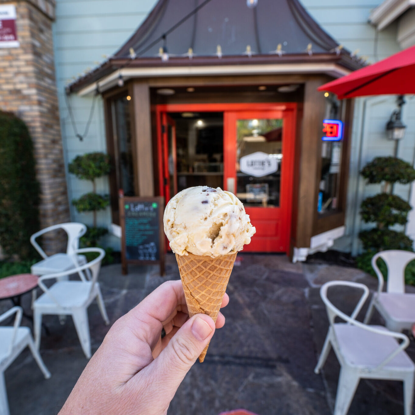 Hand holding a scoop of cookie dough ice cream in a waffle cone in front of Lottie’s Creamery in Danville.