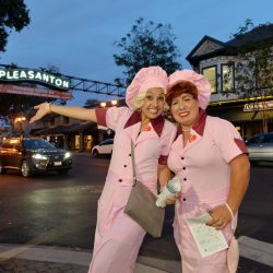 Two ladies in costume pose in front of the Downtown Pleasanton arch at Pleasanton, Ca Halloween Brew Crawl